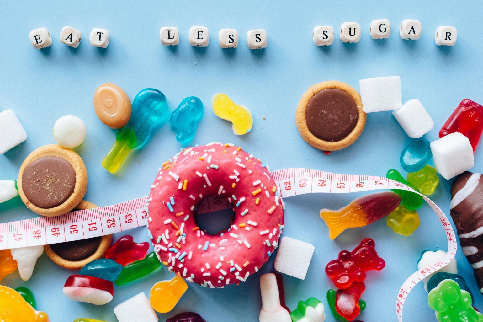 Eat Less Sugar spelled out on dice, sweets, doughnut, biscuits and a measuring tape